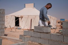 Un jeune Sahraoui construit sa maison en béton devant la tente de sa mère.